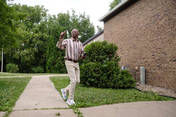 Photo of A man smiling and walking giving a thumbs up to someone outside.